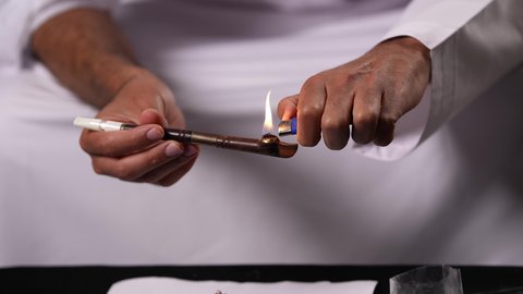 الآثار الضارة للإدمان على التبغ والمخدرات على الصحة، القيام بعادات سلوكية ضارة وتعاطي المواد السامة، المعاناة من الاضطرابات النفسية والمشاكل الصحية، تصوير مقرب ليد رجل عربي خليجي إماراتي يقوم باشعال عقب السجائر