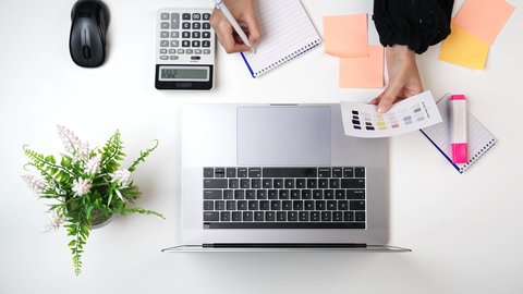 تنظيم الأفكار والملاحظات, استخدام التقنيات الحديثة ، مصممة خليجية تعمل من خلال اللابتوب على مكتب أبيض, وظيفة ومهن سعودية, تصوير مقرب من الأعلى لامراة عربيه خليجيه سعودية لديها خبره بدرجات الألوان ,بيئة عمل مكتبية, خلفية بيضاء