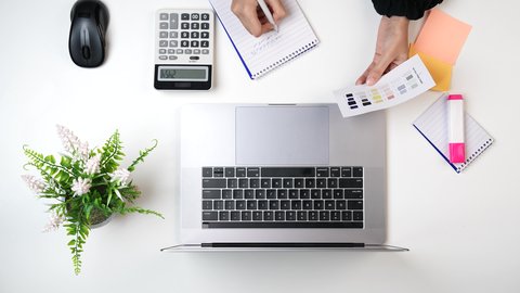 تسجيل الملاحظات على ورق, استخدام التقنيات الحديثة ، مصممة خليجية تعمل من خلال اللابتوب على مكتب أبيض, وظيفة ومهن سعودية, تصوير مقرب من الأعلى لامراة عربيه خليجيه سعودية لديها خبره بدرجات الألوان ,بيئة عمل مكتبية, خلفية بيضاء