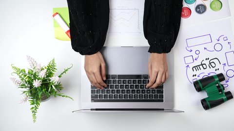 A close-up shot from above of a Saudi Arabian woman with experience in business management, an expert marketer working on a laptop at a white desk, a Saudi job and profession, an office work environment, white background.