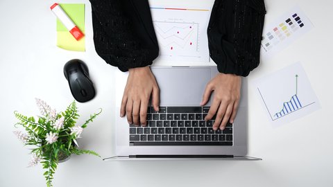 The use of modern technologies, a Gulf designer working on a laptop at a white desk, Saudi jobs and professions, a close-up shot from above of an Arab Gulf Saudi woman with experience in color grading, office work environment, white background.