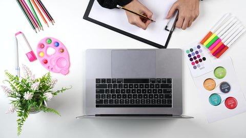 التعلم والابداع وتنمية المهارات, ادوات ومعدات التلوين، نشاطات ترفيهية فنية، تصوير مقرب من الاعلى ليد امراة عربية خليجيه سعودية تقوم بالرسم على اللوحة امام الحاسب المحمول