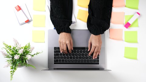 Taking and writing notes, organizing and managing tasks via the laptop, a close-up shot from above of a Saudi Gulf Arab woman's hand pressing the keys of the laptop keyboard, using modern devices and technologies at work.