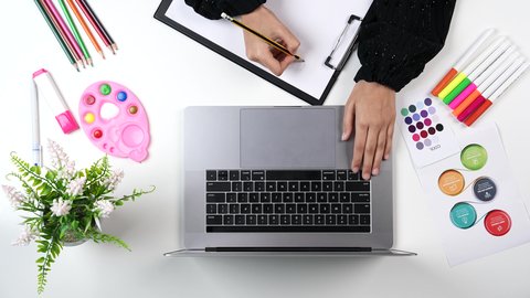 نشاطات ترفيهية فنية، تصوير مقرب من الاعلى ليد امراة عربية خليجيه سعودية تقوم بالرسم على اللوحةامام الحاسب المحمول، ادوات ومعدات التلوين، التعلم والابداع وتنمية المهارات