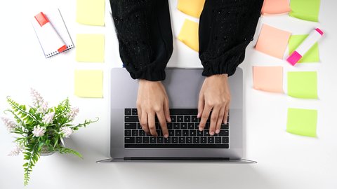 Taking and writing notes, organizing and managing tasks via the laptop, a close-up shot from above of a Saudi Gulf Arab woman's hand pressing the keys of the laptop keyboard, using modern devices and technologies at work.