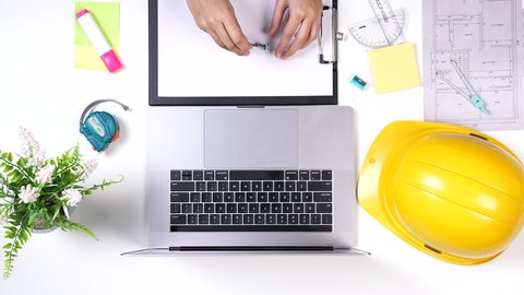 Writing important notes, office work environment, an engineer working on designing buildings using a laptop on a white desk, Saudi jobs and professions, close-up shot from above of a Gulf architectural engineer, white background.