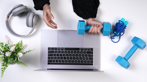 مهنة ووظيفه سعودية , الاهتمام باللياقة البدنية ،تصوير مقرب من الأعلى لمدربة رياضية تعمل من خلال اللابتوب على مكتب أبيض , بيئة عمل مكتبية ، خلفية بيضاء .