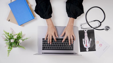 القطاع الطبي بالمملكة العربية السعودية, دمج التكنولوجيا بالطب، مفهوم الرعاية الصحية ،تصوير مقرب من الأعلى لطبيبة خليجية سعودية تعمل على الحاسوب المحمول في العيادة, تقديم الاستشارات الطبية