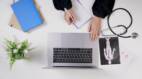 Integrating technology with medicine, the concept of healthcare, the medical sector in the Kingdom of Saudi Arabia, a close-up shot from above of a Saudi Gulf female doctor working on a laptop in the clinic, providing medical consultations.