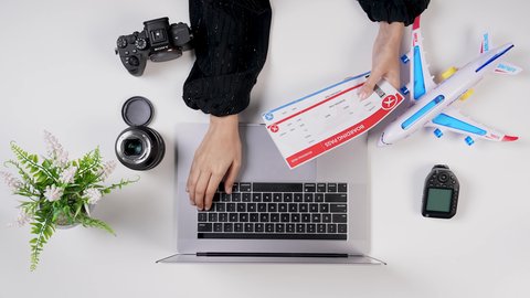 العمل عن بعد ، تصوير مقرب من الأعلى لامراة عربيه خليجيه سعودية تضع معلومات تذاكر الرحلات الى اللابتوب في المطار , بيئة عمل مكتبية , خلفية بيضاء