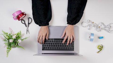 تصميم ورسم الأزياء عن طريق اللابتوب, العمل فى المكتب , مصممة أزياء خليجية سعودية تقوم بالنقر على لوحة مفاتيح اللابتوب , مصممة أزياء مبتكرة , مهنة ووظيفه سعودية , معدات الخياطة