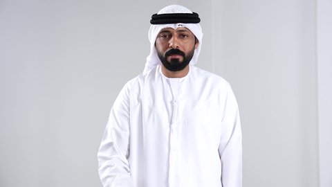 The gesture of patience and caution, giving some time to do something, threatening and warning someone, the concept of patience and deliberation, a close portrait of an Emirati Gulf Arab man wearing a kandura and ghutrah raising his hands with expressions asking for waiting and slowing down, white background.