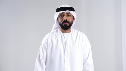 القوة والتحدي والحماس، مفهوم الانجاز وتحقيق الاهداف، بورتريه لرجل  عربي خليجي اماراتي يرتدي الكندورة و الغتره يرفع قبضتيه نحو الأعلى بإيماءات التشجيع، تعابير السرور والسعادة، خلفية بيضاء