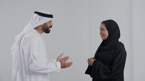 دردشة ومحادثات عائلية, أجواء عائلية مليئة بالحب، الحياة لزوجية الناجحة، مفهوم الترابط الأسري، بورتريه من الجانب لرجل عربي خليجي اماراتي يرتدي الكندورة و الغتره يقوم بالتحدث مع زوجته، ايماءات السعادة و السرور, خلفية بيضاء