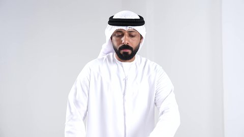 Tracking notifications through modern watches, organizing and monitoring time, a portrait of an Emirati Gulf Arab man wearing a kandura and a white ghutrah looking at a smart watch, white background.