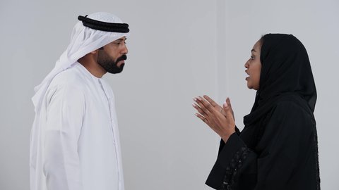 Misunderstanding, a quarrel between spouses, a portrait of an Arab couple from the Gulf, Emiratis wearing traditional attire arguing with each other, family problems, family conflict, crisis in family relationships, white background.