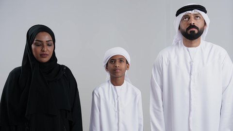 التقرب إلى الله تعالى والرغبة في تحقيق الأمنيات, الدعاء والتضرع والتوسل بإيماءات الخشوع، الترجي والتذلل لرب العالمين, بورترية مقرب لعائلة عربية خليجيه اماراتية ترتدي الزي التقليدي  تنظر إلى الأعلى يرفعون ايديهم باستعطاف, خلفية بيضاء