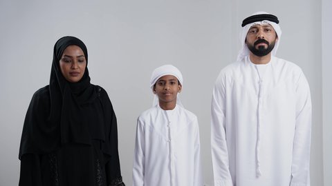 الدعاء والتضرع والتوسل بإيماءات الخشوع، التقرب إلى الله تعالى والرغبة في تحقيق الأمنيات، الترجي والتذلل لرب العالمين, بورترية مقرب لعائلة عربية خليجيه اماراتية ترتدي الزي التقليدي  تنظر إلى الأعلى يرفعون ايديهم باستعطاف, خلفية بيضاء