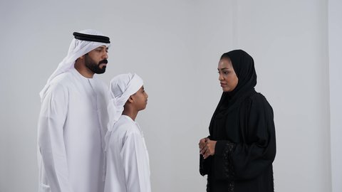 بورتريه لام عربيه خليجيه اماراتية ترتدي العباءه و الحجاب تقوم بنصح ابنها برفقة والده, مفاهيم التربية الأسرية والعلاقات العائلية, نقاش أسري بين الام والابن، ولد عربية خليجي اماراتى يرتدي العمامة يقوم بالتحدث مع والدته, خلفية بيضاء