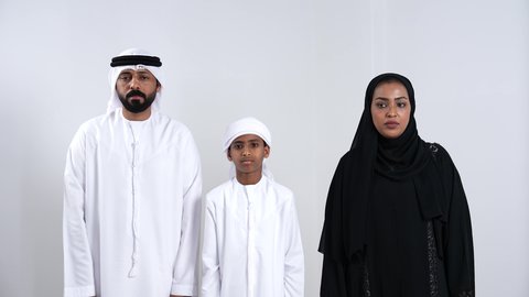 الانزعاج و القهر من الخساره, التفاجؤ من شيء ما, الشعور بالدهشة والصدمة والذهول، بورتريه لرجل عربي خليجي اماراتي يرتدي الكندورة و الغتره ينظر الى الكاميرا يضع يديه على رأسه بإيماءات التعجب و الاندهاش برفقة زوجته و ابنه، خلفية بيضاء