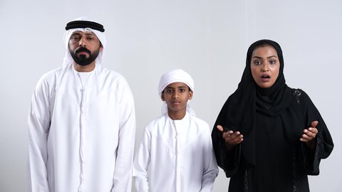 الشعور بالدهشة والصدمة والذهول, التفاجؤ من شيء ما، بورتريه لرجل عربي خليجي اماراتي يرتدي الكندورة و الغتره ينظر الى الكاميرا يضع يديه على رأسه بإيماءات التعجب و الاندهاش برفقة زوجته و ابنه, الشعوربالانزعاج و القهر من الخساره، خلفية بيضاء