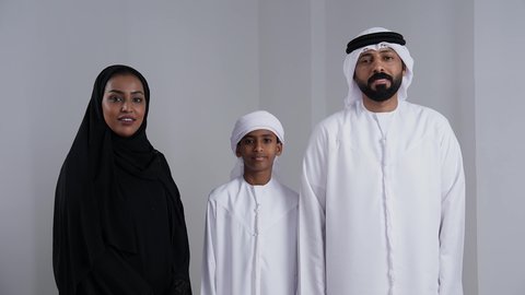 استلام وتسليم المفاتيح، الحصول على رخصة القيادة،, الأجواء العائلية المليئة بالحب, بورتريه لرجل عربي خليجي اماراتي يرتدي الكندورة و الغتره يمسك بيدية مفتاح التحكم عن بعد و ينظر الى الكاميرا بايماءات السعادة و السرور برفقة زوجته و ابنه, خلفية بيضاء