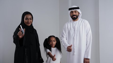 مفهوم الموافقة و القبول, الفرح لامتلاك سيارة جديدة, بورتريه لعائلة عربية خليجيه اماراتية ترتدي الثوب التقليدي تنظر الى الكاميرا بايماءت السعادة و السرور,امراة خليجيه تمسك بيديها مفتاح التحكم عن بعد, خلفية بيضاء