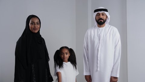 الفرح لامتلاك سيارة جديدة, مفهوم الموافقة و القبول, بورتريه لعائلة عربية خليجيه اماراتية ترتدي الثوب التقليدي تنظر الى الكاميرا بايماءت السعادة و السرور,امراة خليجيه تمسك بيديها مفتاح التحكم عن بعد, خلفية بيضاء