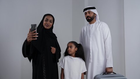 استخدام الأجهزة والتقنيات الحديثة, بورتريه لعائلة عربية خليجيه اماراتية ترتدي الزي التقليدي تقوم بالتقاط صور السيلفي التذكارية بايماءات الفرح والسرور, توثيق اللحظات السعيدة عبر الهاتف المحمول,  رجل عربي خليجي اماراتي يرتدي الكندورة و الغتره يمسك بيده حقيبه سفر استعداد لقيام رحله ترفيهيه, خلفية بيضاء