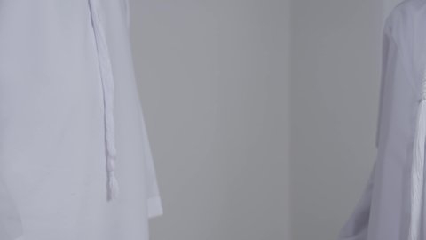 الحب والعطف على الأبناء, مفهوم الرابطة الأبوية والترابط الأسري, تحمل المسؤولية والاعتناء بالأولاد، بورتريه مقرب ليد رجل عربي خليجي اماراتي يرتدي الكندورة  يسمك بيد ابنه، خلفية بيضاء