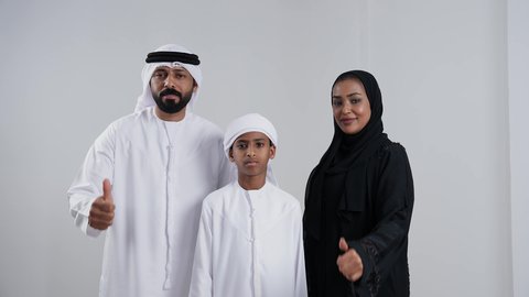 الاعجاب والرضا لتحقيق أمر معين، النظر الى الكاميرا بتعابير السرور, بورترية لعائله عربيه خليجيه اماراتية سمراء ترتدي الزي التقليدي يشعرون بالإعجاب والرضى، رفع اصبع الابهام للأعلى بإيماءات القبول و الموافقة، خلفية بيضاء