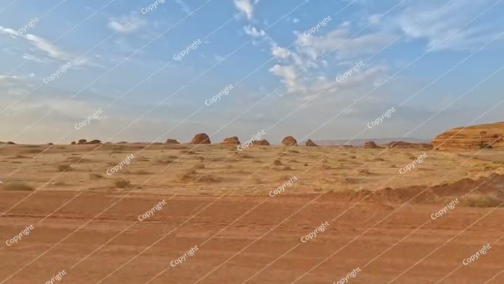 منظر من السيارة أثناء القيادة في منطقة الحجر الأثرية، صحراء مسطحة مع القليل من الأشجار الصغيرة.