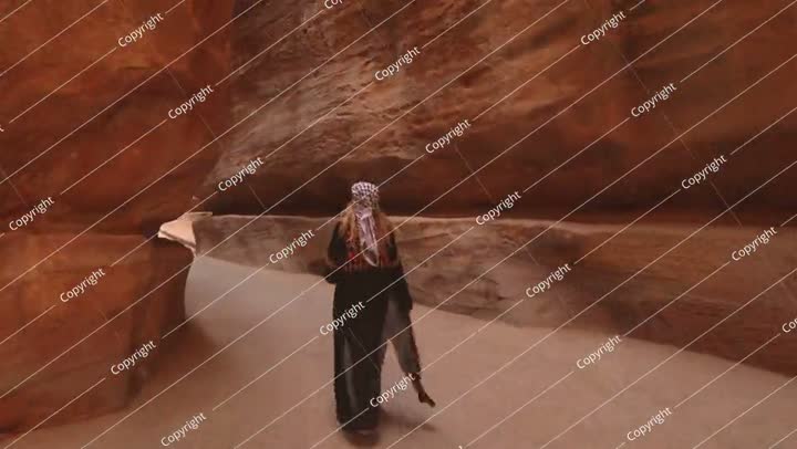 Woman walks through the narrow sandstone canyon known as the Siq, the main