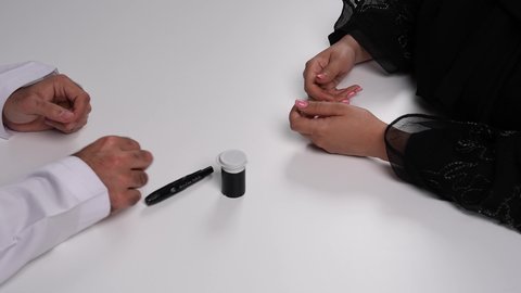 تصوير مقرب لامرأة عربية خليجية إماراتية ترتدي العباءة تقوم بوخز اصبعها, الفحوصات الطبية السريعة لمعرفة نسبة السكر في الدم، استخدام الأجهزة الالكترونية للتحاليل المنزلية، شابة سعودية مصابة بحالة مرضية مزمنة, المتابعة الدورية لمرضى داء السكري, خلفية بيضاء