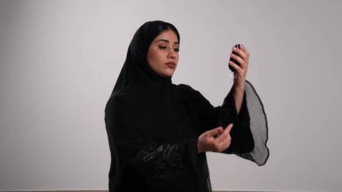 استخدام الأجهزة الالكترونية للتحاليل المنزلية، الفحوصات الطبية السريعة لمعرفة نسبة السكر في الدم،شابة سعودية مصابة بحالة مرضية مزمنة, المتابعة الدورية لمرضى داء السكري, تصوير مقرب لامرأة عربية خليجية إماراتية ترتدي العباءة تقوم بوخز اصبعها, خلفية بيضاء