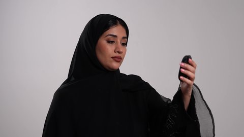 الفحوصات الطبية السريعة لمعرفة نسبة السكر في الدم، استخدام الأجهزة الالكترونية للتحاليل المنزلية، شابة سعودية مصابة بحالة مرضية مزمنة, المتابعة الدورية لمرضى داء السكري, تصوير مقرب لامرأة عربية خليجية إماراتية ترتدي العباءة تقوم بوخز اصبعها, خلفية بيضاء