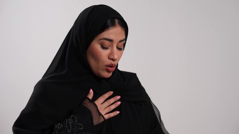 استخدام جهاز الرذاذ الخاص بمرض الربو، الشعور بالاختناق وضيق في النفس، إمرأة سعودية مصابة بتضرر في مجرى الهواء، أجهزة استنشاق خاصة بمرضى الجهاز التنفسي والرئتين، تصوير مقرب لشابة عربية خليجية إماراتية محجبة ترتدي العباءة تعاني من أزمة تنفس تحسسية، خلفية بيضاء