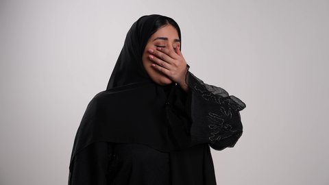 إيماءات التعب والإرهاق والحاجة لأخذ قسط من الراحة، أهمية الخلود للنوم باكرا واتباع نظام صحي، الإحساس بالملل والخمول، امرأة سعودية تضع يدها أمام فمها بتعابير النعاس والكسل، تصوير مقرب لشابة عربية خليجية إماراتية محجبة ترتدي العباءة تقوم بالتثاؤب، خلفية بيضاء