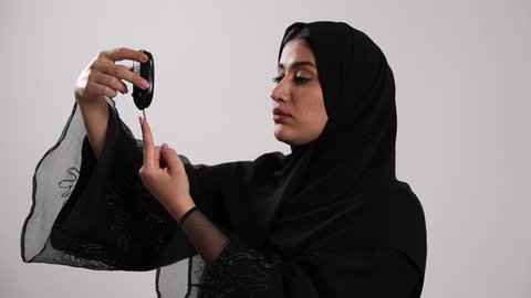 تصوير مقرب لامرأة عربية خليجية إماراتية ترتدي العباءة تقوم بوخز اصبعها, الفحوصات الطبية السريعة لمعرفة نسبة السكر في الدم، استخدام الأجهزة الالكترونية للتحاليل المنزلية، شابة سعودية مصابة بحالة مرضية مزمنة, المتابعة الدورية لمرضى داء السكري, خلفية بيضاء
