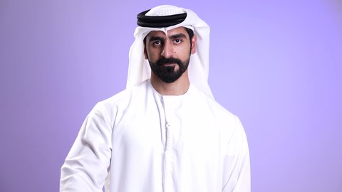 Satisfaction with the result, excellence, and distinction, gestures of agreement and acceptance, a close-up image of an Emirati Gulf Arab man wearing the Emirati kandura and white ghutrah, raising his thumb up with expressions of admiration and satisfaction, with a purple background.