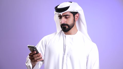 تبادل الأخبار والأحاديث, إجراء مكالمة فيديو مع الأهل والأصدقاء عبر الهاتف المحمول، ايماءات السلام والترحيب, تصوير مقرب لشاب عربي خليجي إماراتي يرتدي الكندورة والغترة يقوم ببث مباشر على مواقع التواصل، استخدام التقنيات الحديثة والمتطورة, خلفية موف