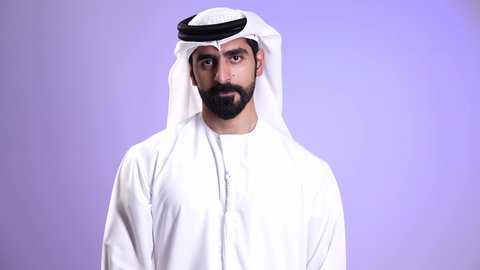 مفهوم الاستقبال والترحيب, إلقاء التحيه والسلام, التعارف و الصداقه وتكوين علاقات, تصوير مقرب لشاب عربي خليجي اماراتي يرتدي الكندورة والغترة البيضاء يقوم بالاشارة بيديه للمصافحة بإيماءات السرور والبشاشة، خلفية موف