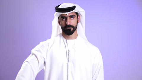 الشعور بالانزعاج من شيء ما، تعابير الرفض وعدم القبول، تصوير مقرب لرجل عربي خليجي امارتي يرتدي الكندورة و الغترة يشير بإصبعه الابهام الى الأسفل، النظر غلى الكاميرا بإيماءات عدم الاعجاب والتقييم السلبي، خلفية موف