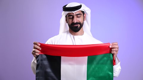 ذكرى استقلال الإمارات العربية المتحدة في 2 ديسمبر، تصوير مقرب لرجل عربي خليجي اماراتي يرتدي الكندورة والغترة يحمل علم الإمارات ، يوم العلم الاماراتي 3 نوفمبر، الفخر بالانتماء للوطن، الاعياد والمناسبات الوطنية، خلفية موف