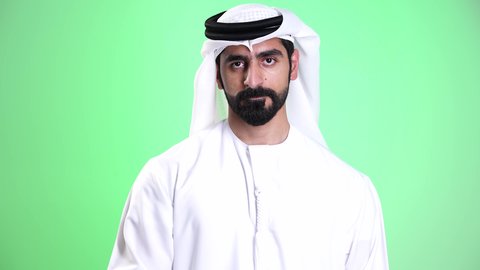 مفهوم الصبر والتريث والتأن، تصوير مقرب لشاب عربي خليجي اماراتي يرتدي الكندورة والغترة يرفع يده بإيماءات طلب الإنتظار، النظر إلى الكاميرا بتعابير الجدية، الهدوء وإمهال بعض الوقت، التهديد و التوعد لشيء ما، خلفية خضراء، كروما