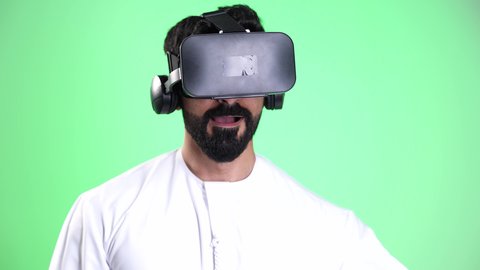 ايماءات الاندماج والدهشة، مفهوم التطور التقني التكنولوجي, التفاعل مع العالم الخيالي، الاستمتاع بمشاهدة شيء ما بنظارات في آر ثلاثية الابعاد، تصوير مقرب لرجل عربي خليجي إماراتي يرتدي الكندورة والغترة يقوم بمحاكاة الواقع الافتراضي،كروما، خلفية خضراء