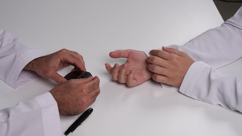 ضرورة التحليل الدوري لمرضى داء السكري, الإصابة بالحالات المرضية المزمنة, تصوير مقرب علوي لرجل عربي خليجي إماراتي يقوم بفحص نسبة السكر في الدم لشخص آخر, الرعاية الصحية والفحوصات الطبية السريعة, الأجهزة الالكترونية الحديثة للتحاليل المنزلية، خلفية بيضاء