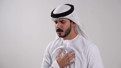 الشعور بالاختناق وصعوبة وضيق في النفس، استخدام جهاز الرذاذ الخاص بمرض الربو، الإصابة بتضرر في مجرى الهواء، أجهزة استنشاق خاصة بمرضى الجهاز التنفسي والرئتين، تصوير مقرب لشاب عربي خليجي إماراتي يرتدي الكندورة والغترة يعاني من أزمة تنفس تحسسية، خلفية بيضاء