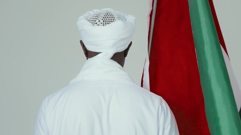 حب الوطن والاعتزاز به، الاحتفال بالاستقلال ١ يناير، استذكار اليوم الوطني السوداني ١٩٥٦ م، بورتريه من الخلف لرجل عربي سوداني يرتدي الجلابية والشال والعمامه البيضاء يضع على كتفيه علم السودان، خلفية بيضاء