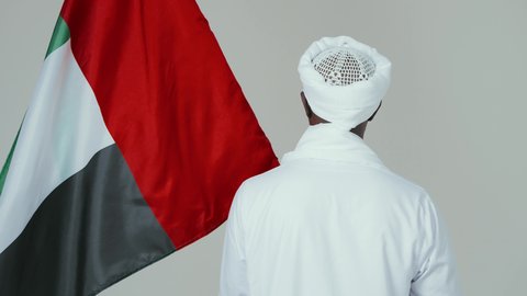 Love of the homeland and pride in it, celebrating independence on January 1, commemorating Sudan's National Day in 1956, a portrait from behind of a Sudanese Arab man wearing a jalabiya, shawl, and white turban, draping the Sudanese flag over his shoulders, with a white background.